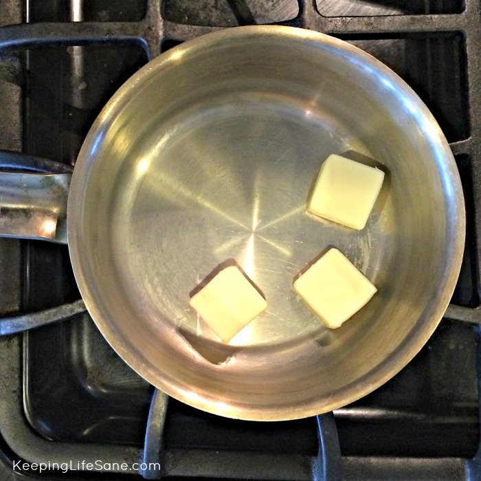 overhead view of stainless steel pot on stove with 3 pats of butter