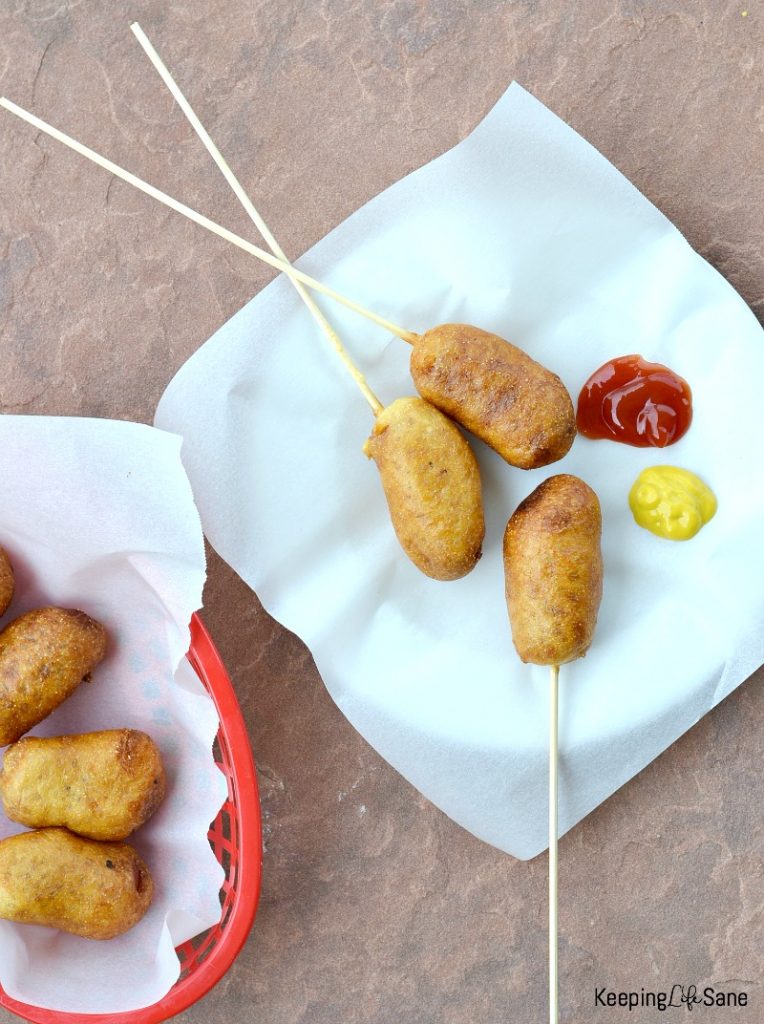 overhead view of homemade corn dogs on white parchment paper and mustard and ketchup