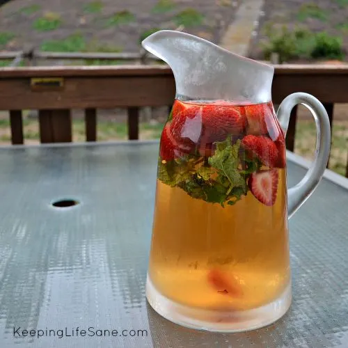 pitcher of iced tea with strawberries and mint sitting on an outside table