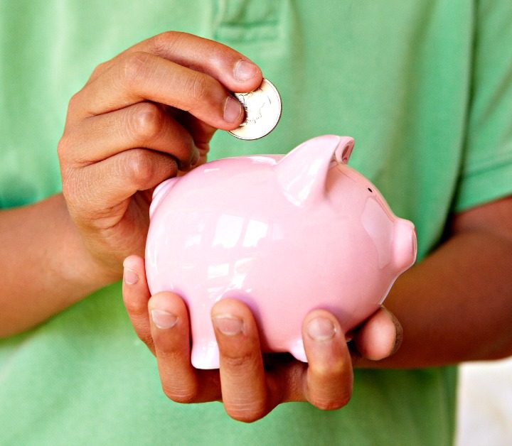boy in green shirt holding pink piggy bank and putting in a quarter