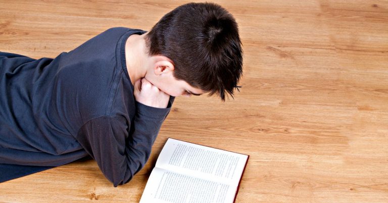 boy lying on hardwood floor and reading a book