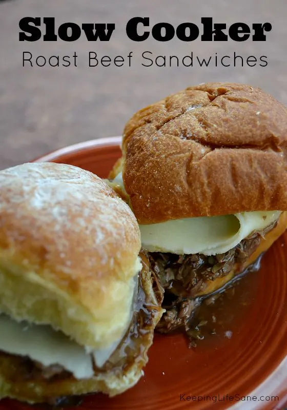 two slider roast beef sandwiches on dark red plate with meat adnd cheese and gravy dripping out.
