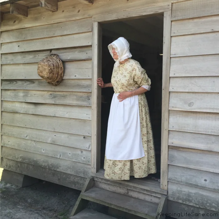 Lady wearing 1800's dress in doorway of wood house