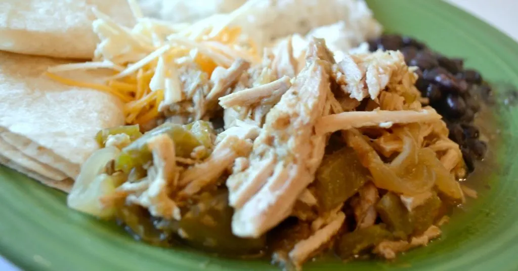 rice, tortillas, black beans, shredded cheese and pork in salsa verde on green plate.