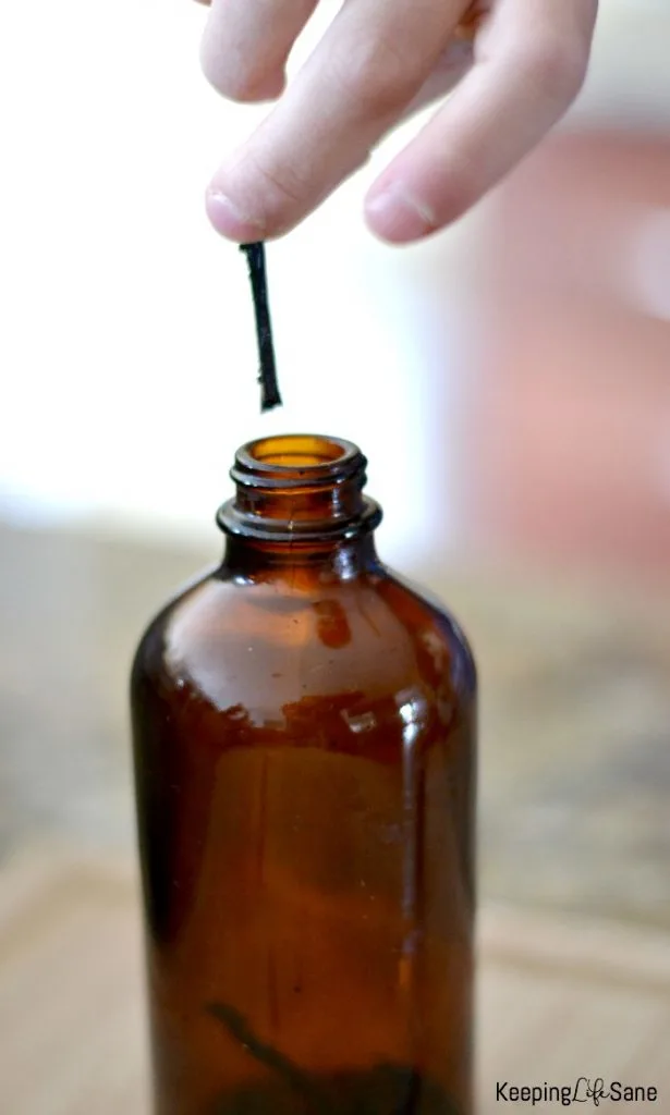 Vanilla bean being put in a brown bottle