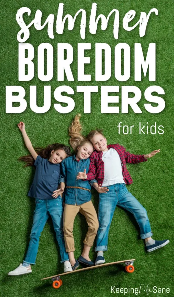 3 kids lying on green grass with feet on skateboard.