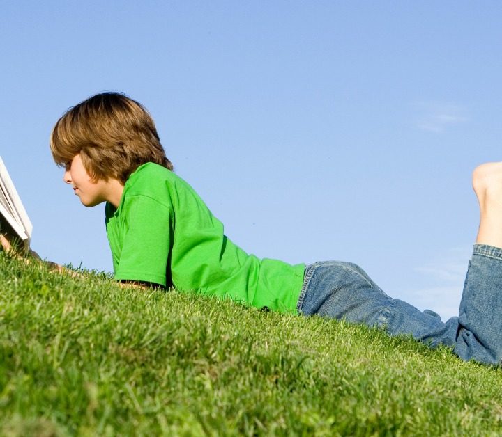 boy laying on grass in jeans and green shirt reading a book