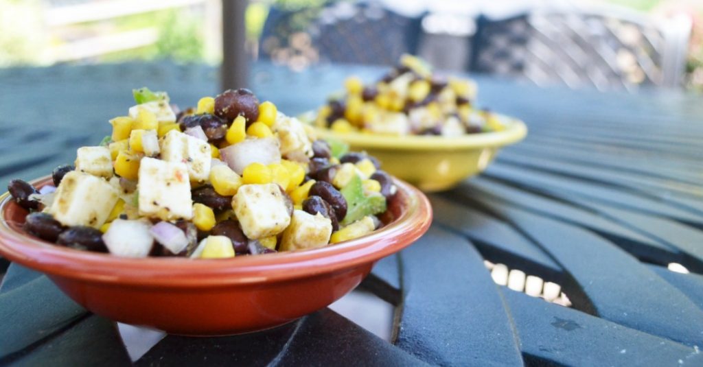 Mexican corn black bean salad in a red and yellow bowl on an outside iron table