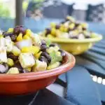 Mexican corn black bean salad in a red and yellow bowl on outside iron table