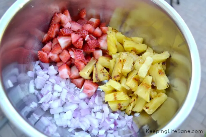 stainless steel bowl with chopped red onions, grilled pineapple and chopped strawberries