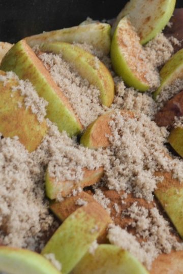 Black slow cooker pot with pork roast with granny smith apples on top and brown sugar