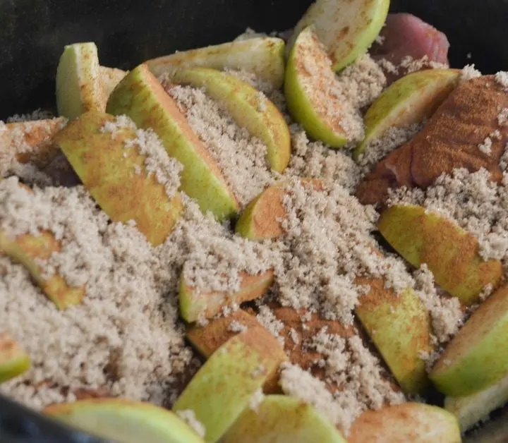 Black slow cooker pot with pork roast with granny smith apples on top and brown sugar