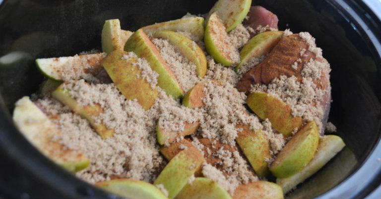Black slow cooker pot with pork roast with granny smith apples on top and brown sugar