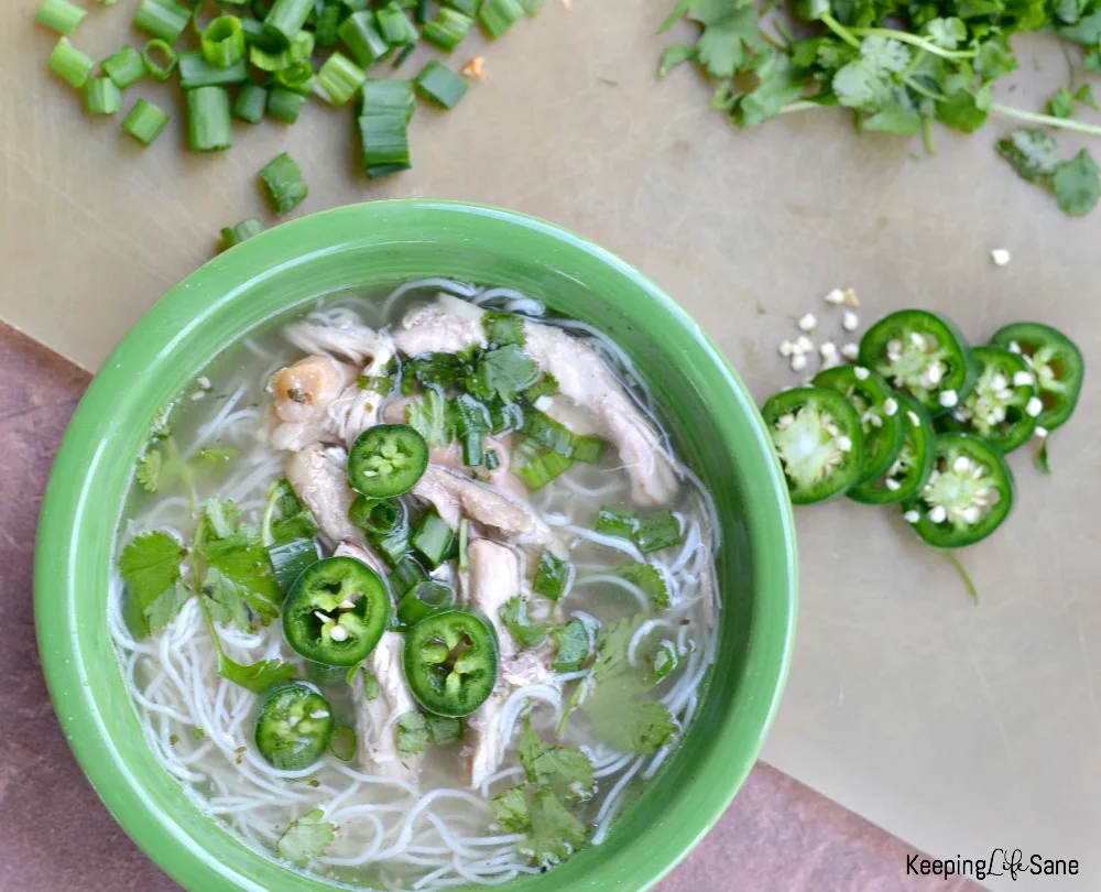 overhead view of EASY chicken pho in green bowl with noodles, chicken, cilantro, and jalapeños