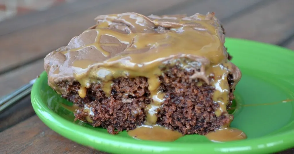 close up of chocolate cake with chocolate icing with caramel syrup oozing out on green plate