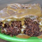 close up of chocolate cake with chocolate icing with caramel syrup oozing out on green plate