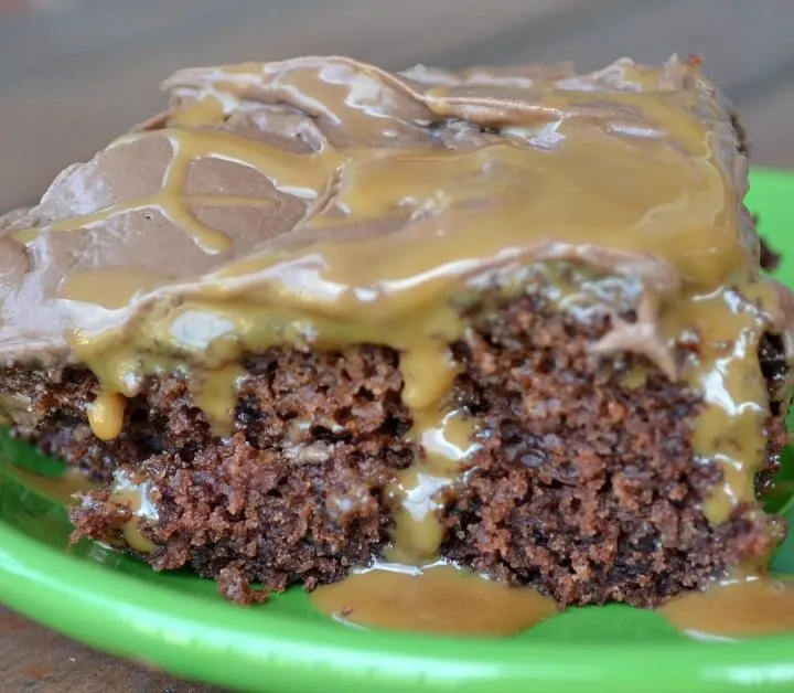 close up of chocolate cake with chocolate icing with caramel syrup oozing out on green plate