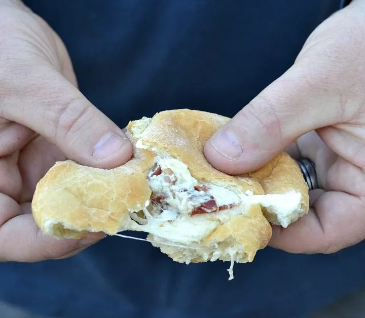 Hands pulling apart bacon bomb with melty cheese and bacon