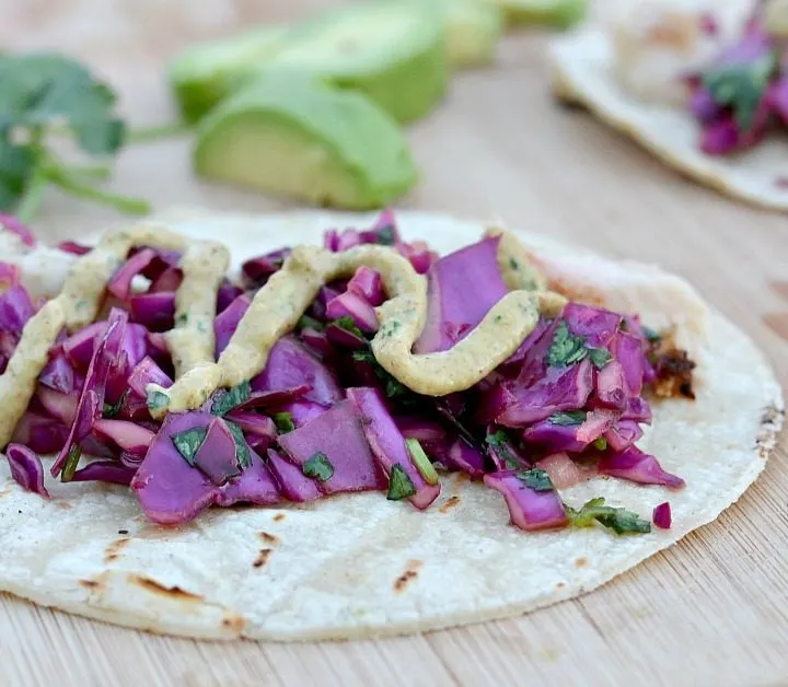 fish tacos on tortilla with red cabbage and cilantro and avocados