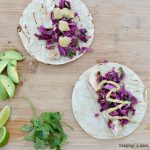 overhead view of tortilla of fish tacos with red cabbage and cilantro and avocados