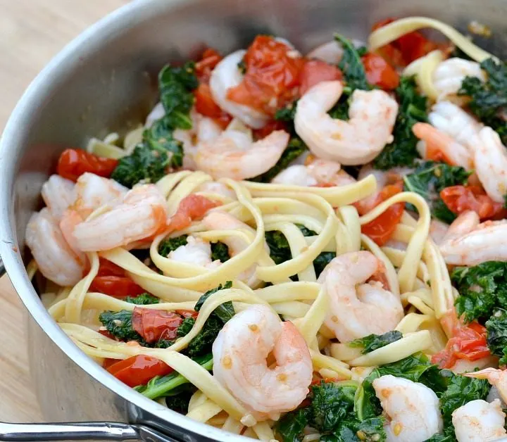 large pot filled with cooked kale, shrimp, red cherry tomatoes and fettuccine