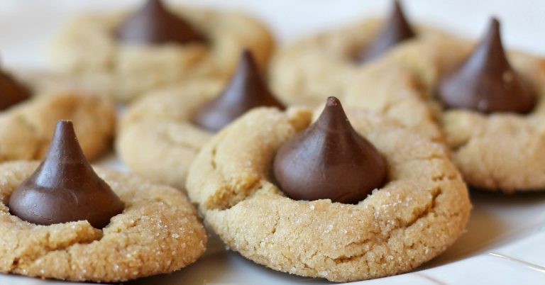 close up of peanut butter cookies with a hershy kiss in the middle on white plate