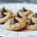 close up of peanut butter cookies with a hershy kiss in the middle on white plate