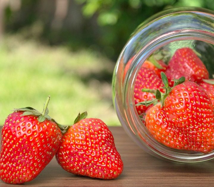 Fresh strawberries outside in a jar that's tipped over and then 2 berries sitting beside it