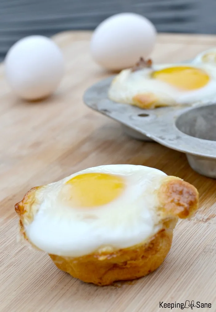 crescent roll egg cup on cutting board with muffin pan and whole eggs in background