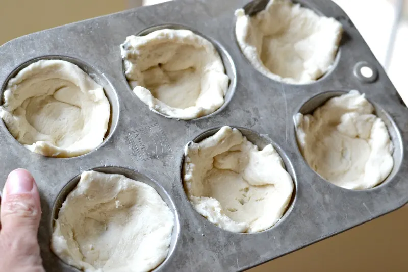muffin tin show with crescent roll dough pressed in