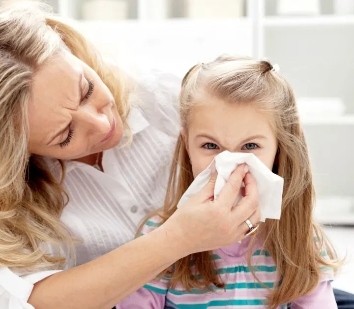 girl with long hair with mom holding a tissue so she can blow her nose