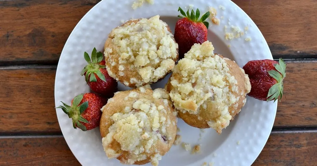 overhead view of white plate with three eggless strawberry muffins with real red strawberry off to the sides