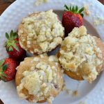 overhead view of white plate with three strawberry muffins with real red strawberry off to the sides