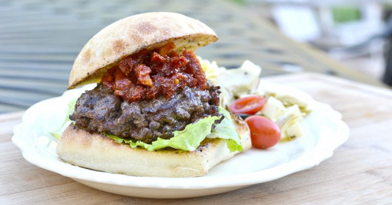 white platter with burger with lettuce and sun dried tomatoes.