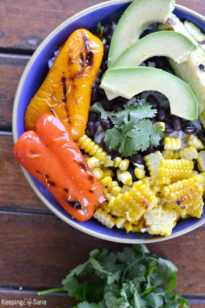 overhead view of burrito bowl with grilled corn, avocados, peppers, with cilantro, black beans and sliced avocado