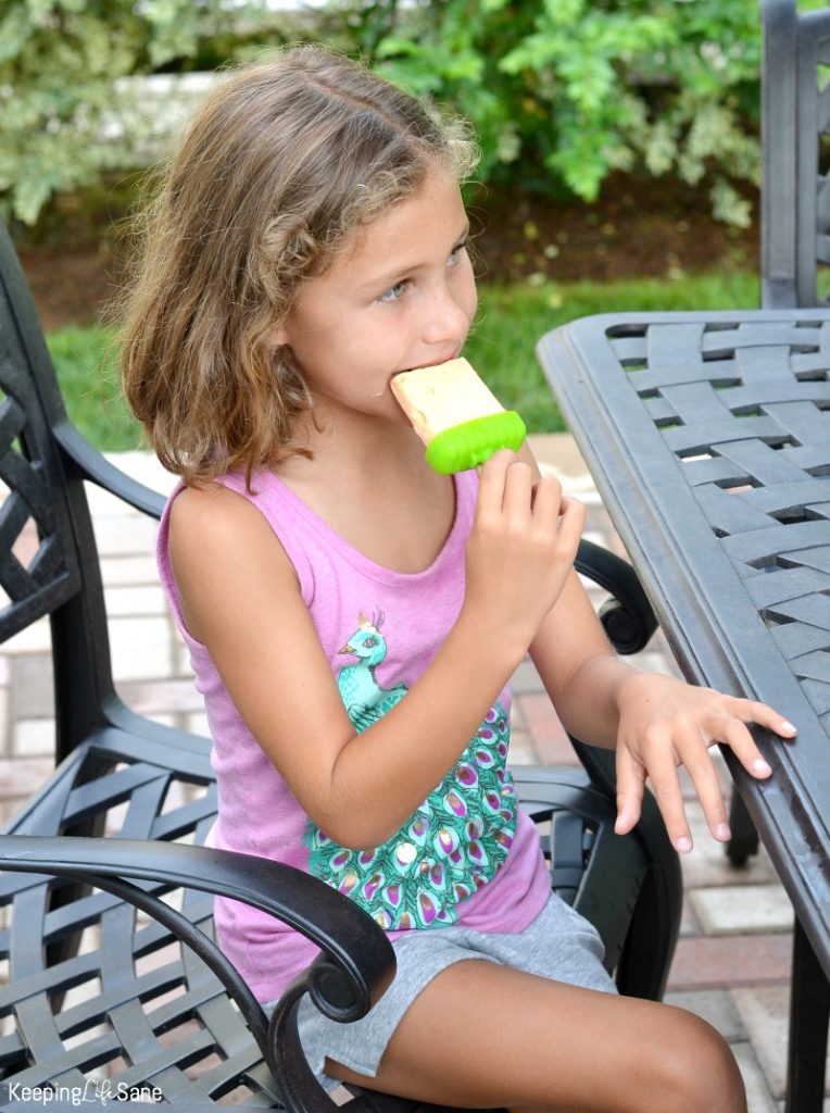 brown haired girl in purple shirt eating creamsicle