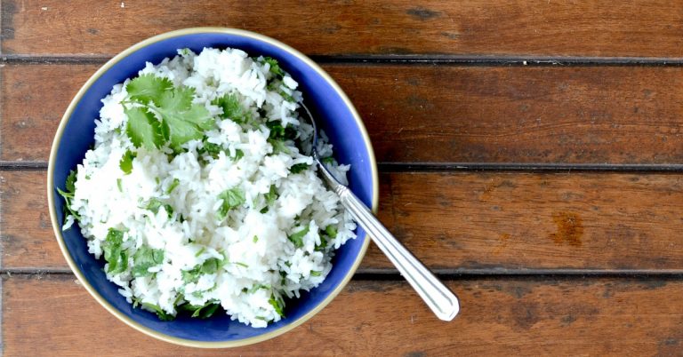 overhead view of cilantro lime rice in the rice cooker placed in blue bowl with spoon
