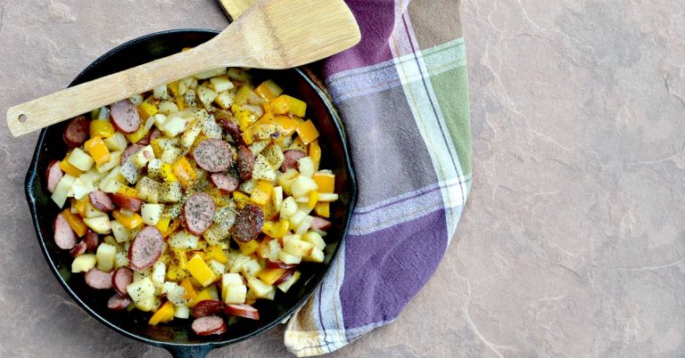 Overhead view of potatoes, sausage, pepper and onion in cast iron skillet with a wooden spoon