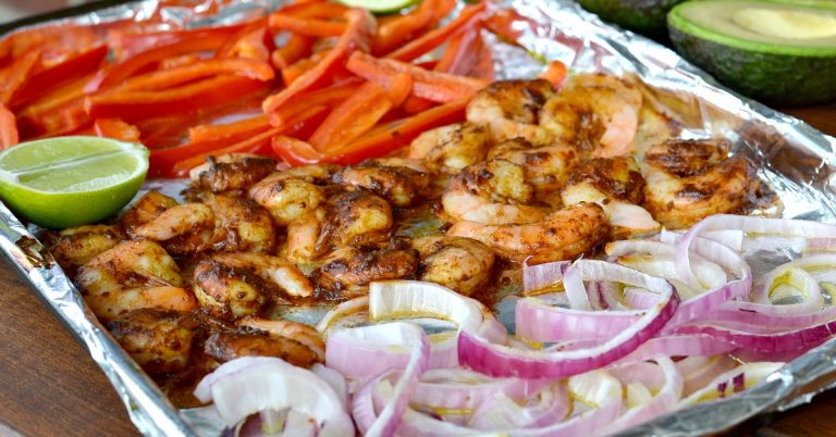 Closeup view of cooked shrimp, onions, red peppers and lime on foil line baking sheet