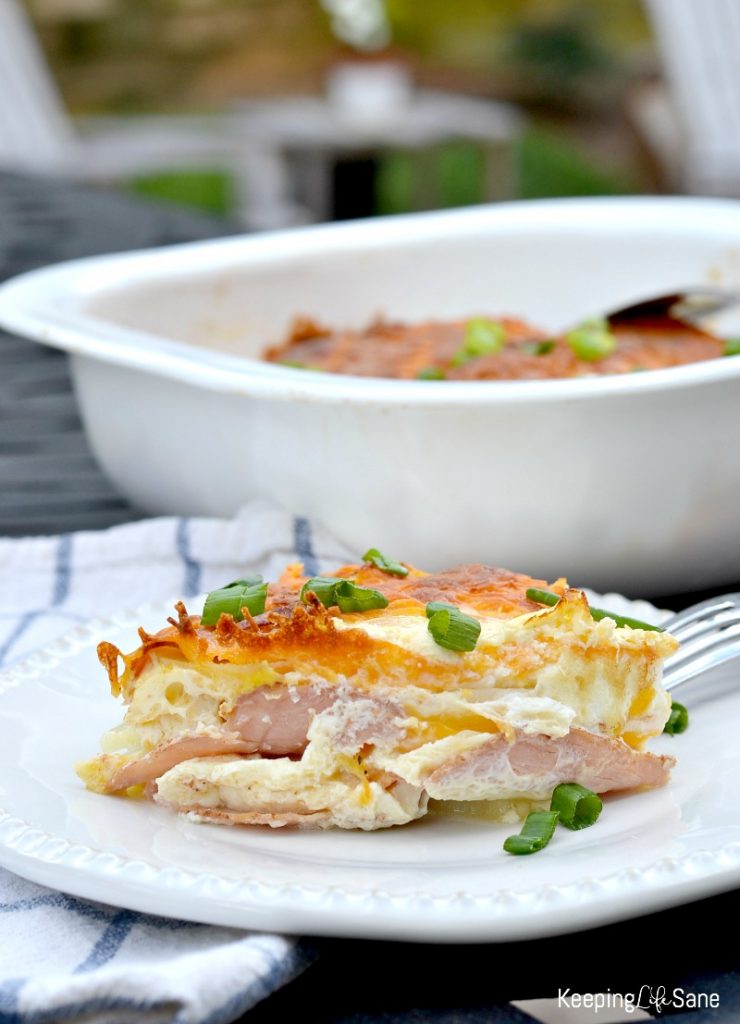 ham cheese potato bake on white plate with green onions on top, white casserole dish in the background