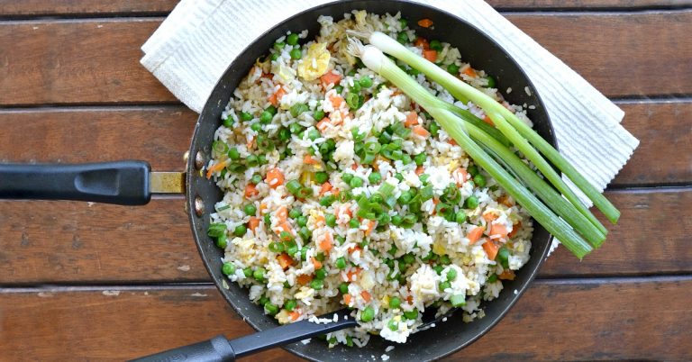 Overhead view of wok with vegetable fried rice with green onions laying on the side of the pot
