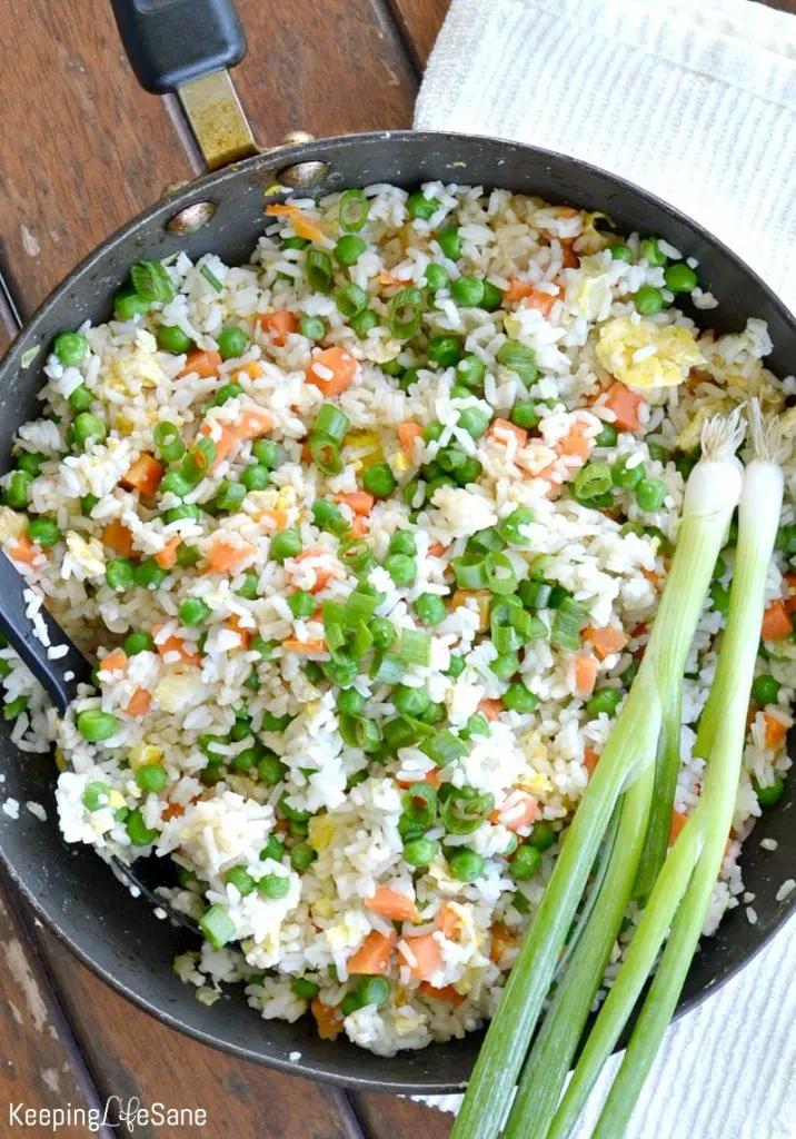 Overhead view of wok with vegetable fried rice with green onions laying on the side of the pot