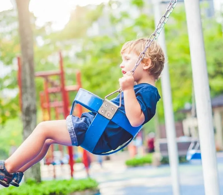 little boy with blond hair swinging at playground in a toddler swing