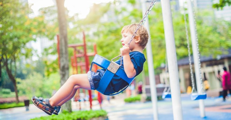 little boy with blond hair swinging at playground in a toddler swing