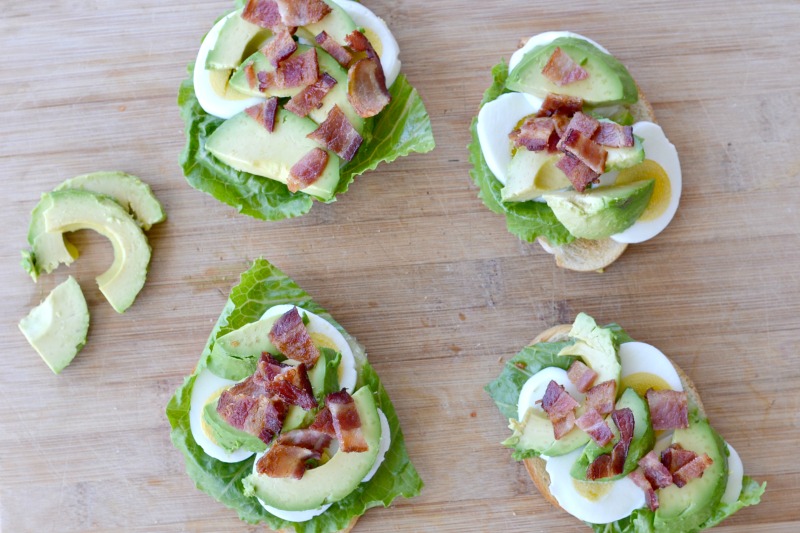 overhead view of toast with lettuce, hard boil eggs, gree avocados with bacon on top