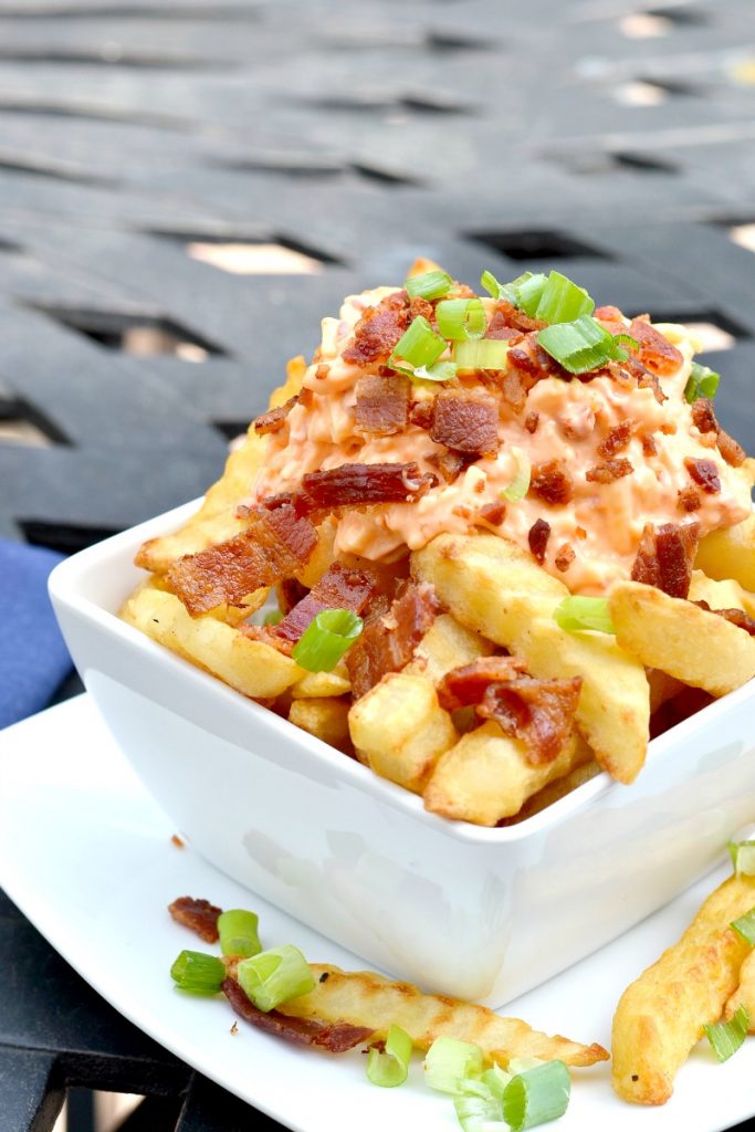 closeup of cheese fries in white bowl pile high with french fries with pimento cheese on top with crumbled bacon and green onions