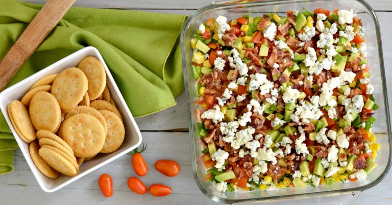 overhead view of Cobb Dip in square glass container with crackers in white bowl with a green napkin