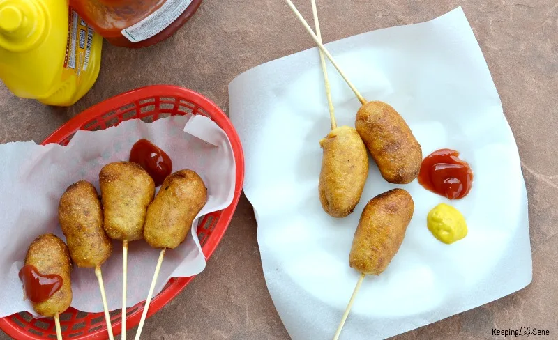 overhead view of homemade mini corn dogs on white parchment paper and mustard and ketchup