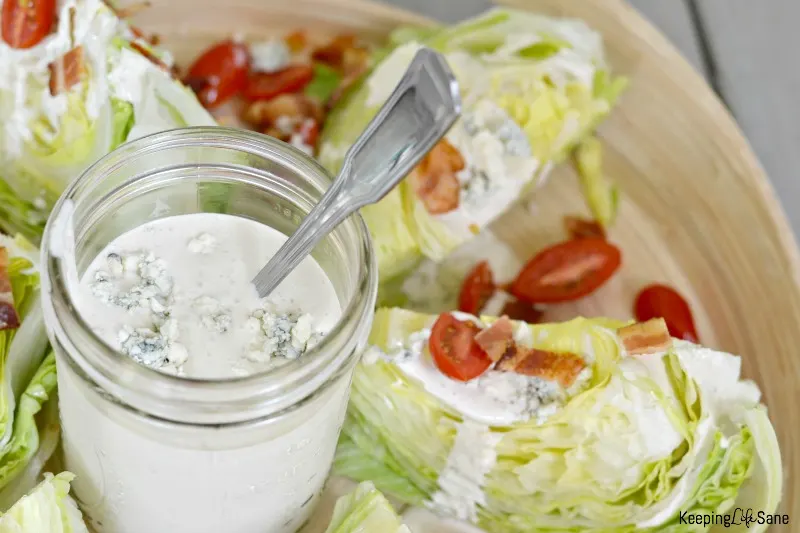 blue cheese salad dressing in jar on wood platter with wedge salad with cherry tomatoes