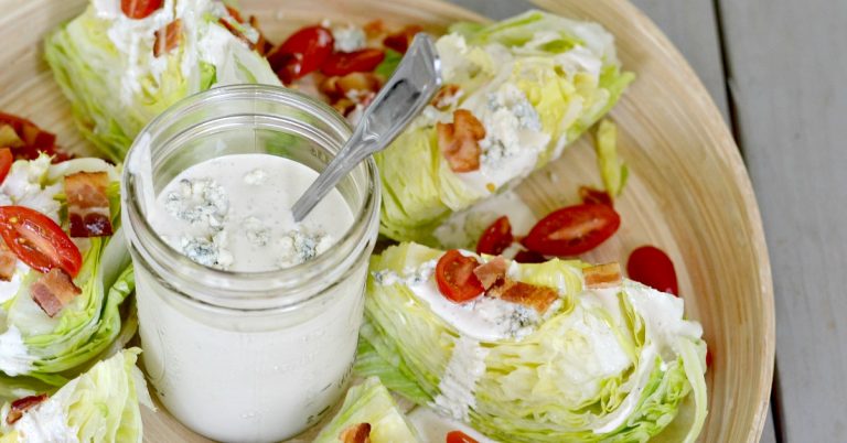 blue cheese salad dressing in jar on wood platter with wedge salad with bacon and cherry tomatoes